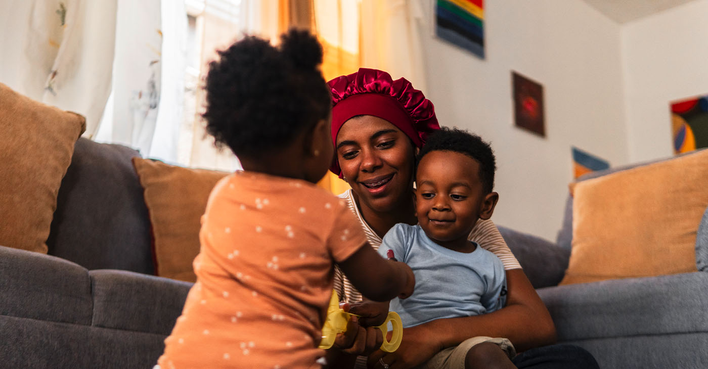 Happy mother spending quality time with her adorable baby daughter and son, playing together on the floor in their cozy living room