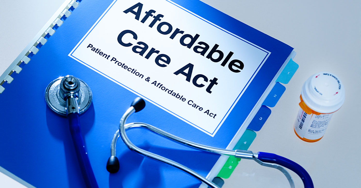 Still life of a manual handbook for the Patient Protection and Affordable Care Act with a stethoscope and prescription medication bottle. The manual is open to the title page, The open enrollment of the Affordable Care Act of the United States offers a health insurance program for all the U.S. citizens across the country.