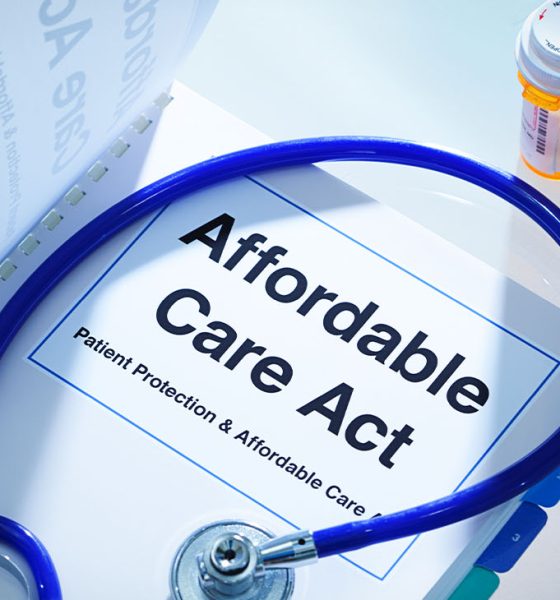 Still life of a manual handbook for the Patient Protection and Affordable Care Act with a stethoscope and prescription medication bottle. The manual is open to the title page, The open enrollment of the Affordable Care Act of the United States offers a health insurance program for all the U.S. citizens across the country.