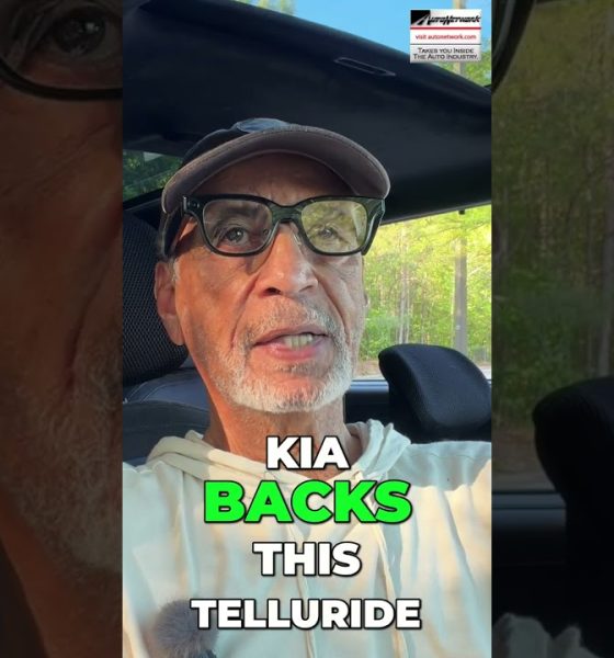 Man wearing cap and glasses sits in a car, outdoor light behind him; overlaid text reads 'KIA BACKS THIS TELLURIDE'.