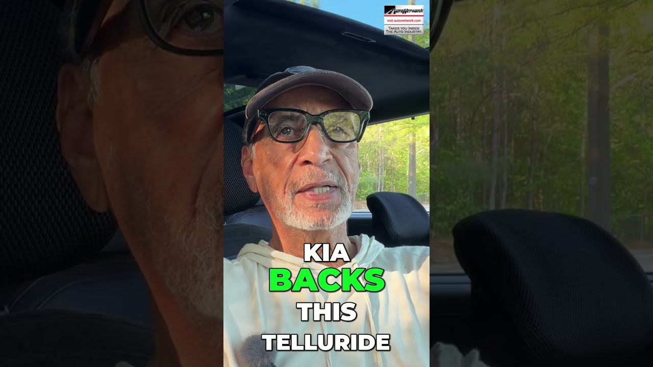 Man wearing cap and glasses sits in a car, outdoor light behind him; overlaid text reads 'KIA BACKS THIS TELLURIDE'.