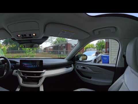 Interior of a modern car viewed from the passenger side, showing dashboard with touchscreen, steering wheel, and sunroof, with street outside the windows.