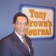 Tony Brown poses in front of the Tony Brown's Journal logo. Brown, who died June 17 at age 93, transformed Black public affairs television and influenced generations of journalists through his groundbreaking broadcast career.