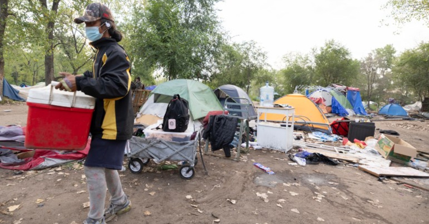Aug 5, 2026, Saint Paul – A resident of the Pigs Eye encampment carries items out of it. Credit: Chris Juhn