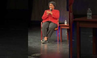 Stacey Abrams speaking at a podium at Harris-Stowe State University about democracy, voting, and leadership.