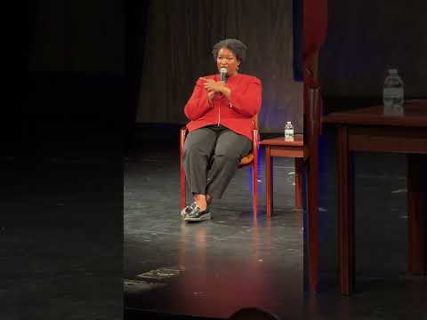 Stacey Abrams speaking at a podium at Harris-Stowe State University about democracy, voting, and leadership.