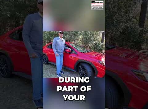Auto mechanic inside a car demonstrating how to turn off music to listen for tire noise during a vehicle test drive.